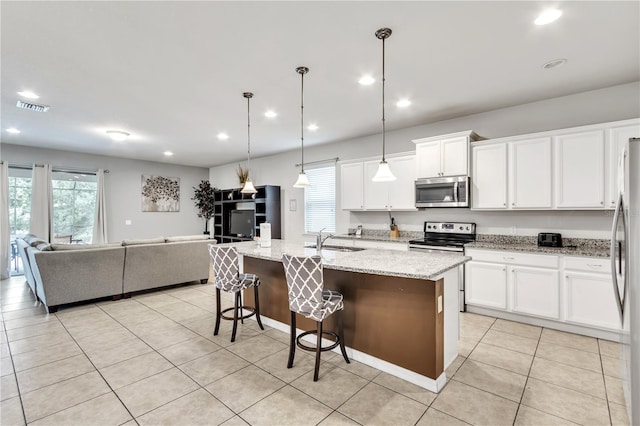 kitchen featuring stainless steel appliances, white cabinets, sink, light stone counters, and a center island with sink