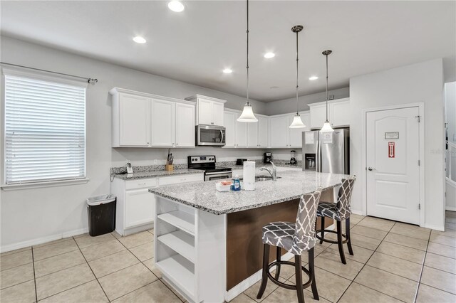 kitchen with appliances with stainless steel finishes, white cabinets, a center island with sink, and light tile patterned floors