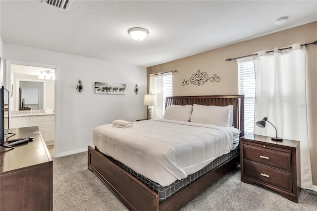 bedroom featuring light colored carpet, visible vents, a textured ceiling, ensuite bath, and baseboards