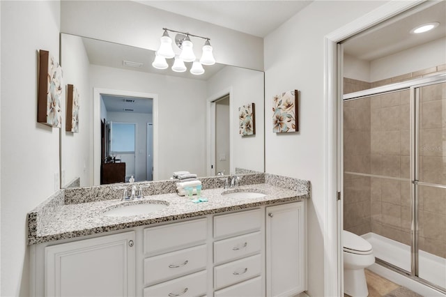 bathroom featuring a shower with door, toilet, and dual bowl vanity