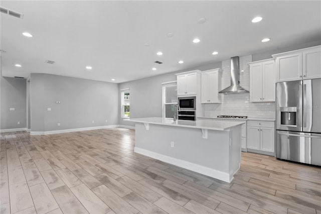 kitchen with built in microwave, white cabinets, a kitchen island with sink, stainless steel fridge with ice dispenser, and wall chimney range hood