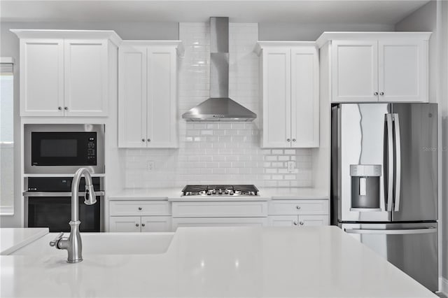 kitchen featuring white cabinetry, appliances with stainless steel finishes, wall chimney range hood, and decorative backsplash