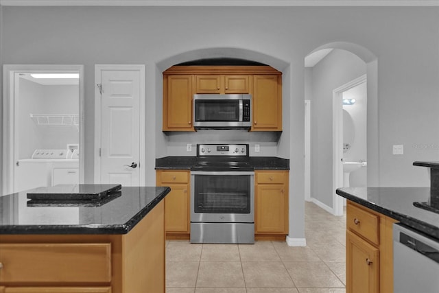 kitchen with dark stone counters, stainless steel appliances, a center island, light tile patterned floors, and independent washer and dryer