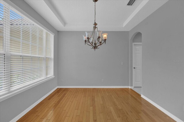 unfurnished room featuring an inviting chandelier, light wood-type flooring, and a raised ceiling