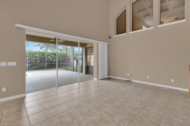 empty room with light tile patterned floors, ceiling fan, and a towering ceiling