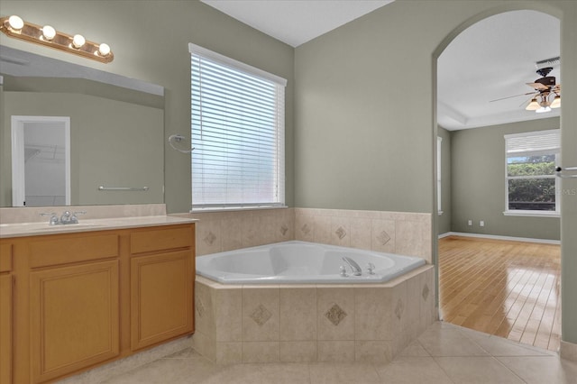 bathroom with a relaxing tiled tub, hardwood / wood-style floors, vanity, and ceiling fan