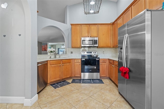 kitchen with appliances with stainless steel finishes, sink, backsplash, high vaulted ceiling, and light tile patterned floors