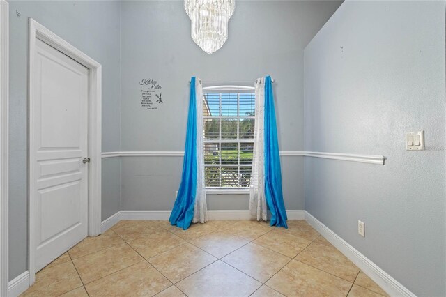 tiled spare room with a notable chandelier and baseboards