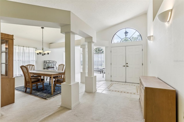 entrance foyer with lofted ceiling, ornate columns, a textured ceiling, light carpet, and a notable chandelier