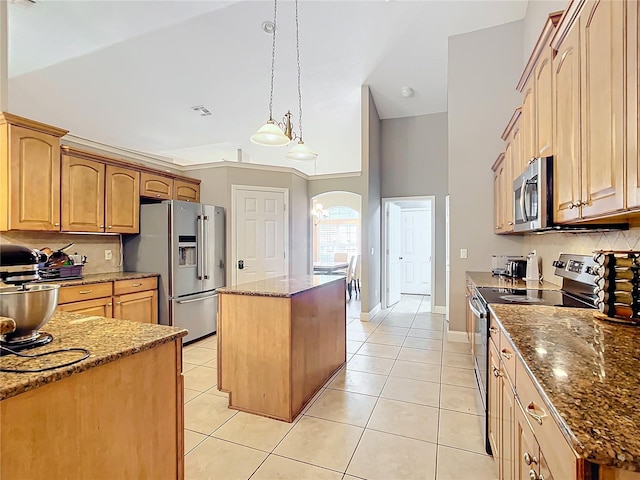 kitchen featuring appliances with stainless steel finishes, dark stone counters, backsplash, a kitchen island, and light tile patterned flooring