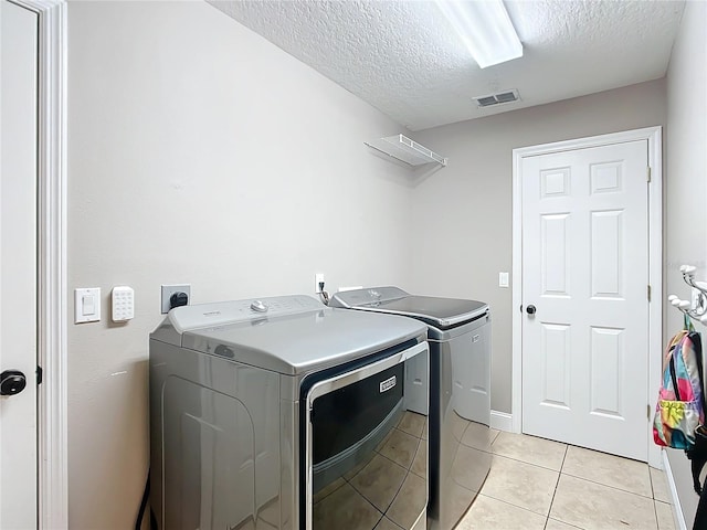 laundry room with washer and clothes dryer, a textured ceiling, and light tile patterned floors