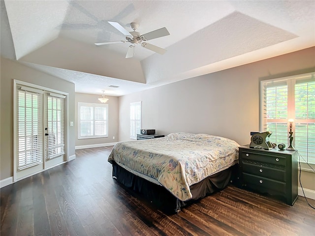 bedroom with ceiling fan, access to outside, a textured ceiling, dark hardwood / wood-style flooring, and a raised ceiling