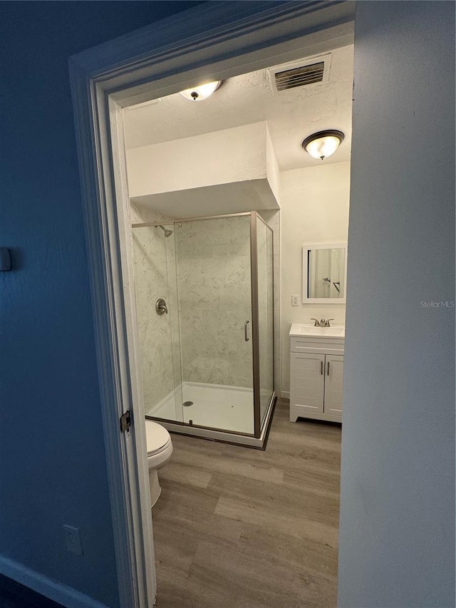 full bathroom with visible vents, a shower stall, toilet, wood finished floors, and vanity