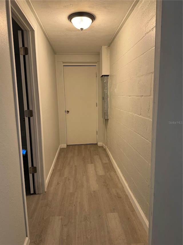 hallway with concrete block wall, wood finished floors, baseboards, and a textured ceiling