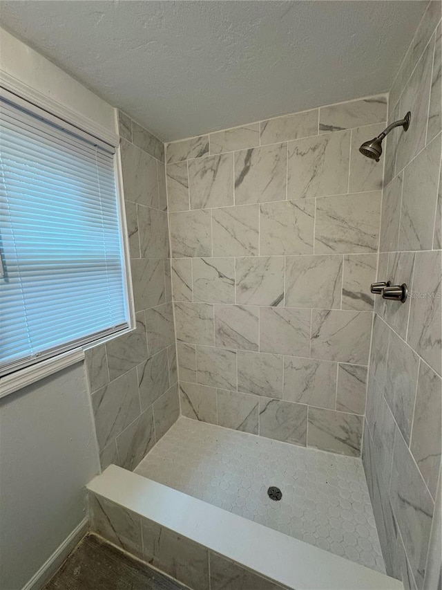 full bathroom featuring a tile shower, a textured ceiling, and baseboards