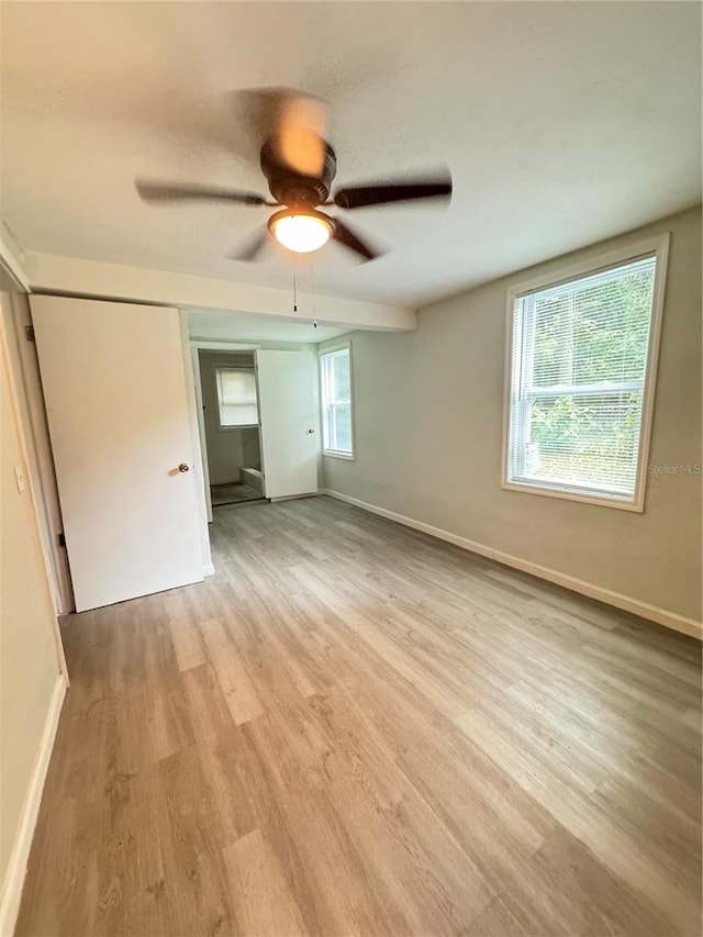 unfurnished bedroom featuring multiple windows, light wood-style floors, and baseboards