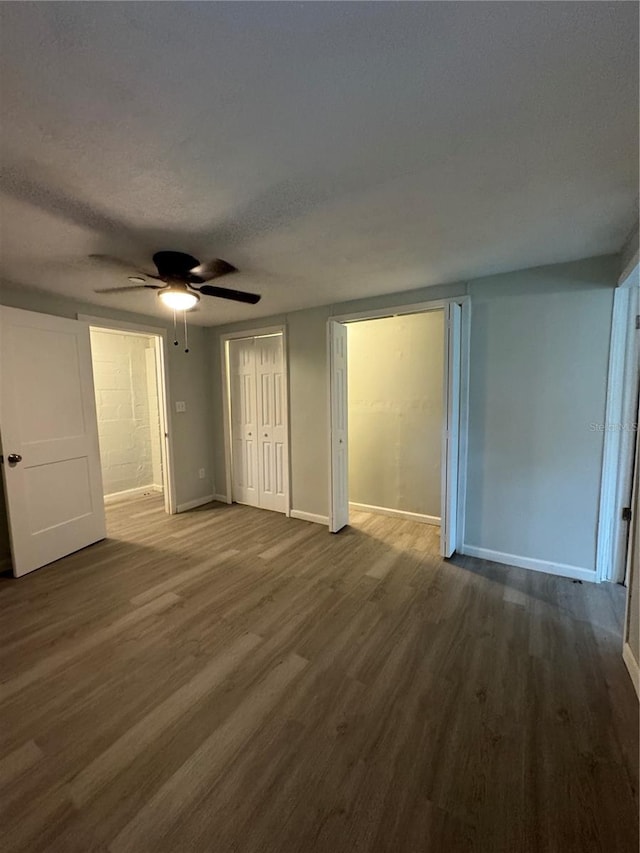 unfurnished bedroom featuring dark wood finished floors, a textured ceiling, baseboards, and a ceiling fan