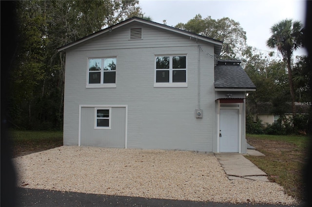 back of house featuring brick siding and a shingled roof