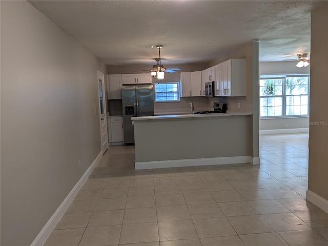 kitchen with stainless steel appliances, white cabinets, kitchen peninsula, light tile patterned flooring, and ceiling fan