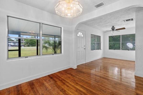 empty room featuring arched walkways, visible vents, baseboards, and wood finished floors