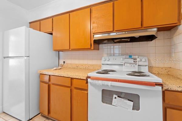 kitchen featuring under cabinet range hood, white appliances, and backsplash