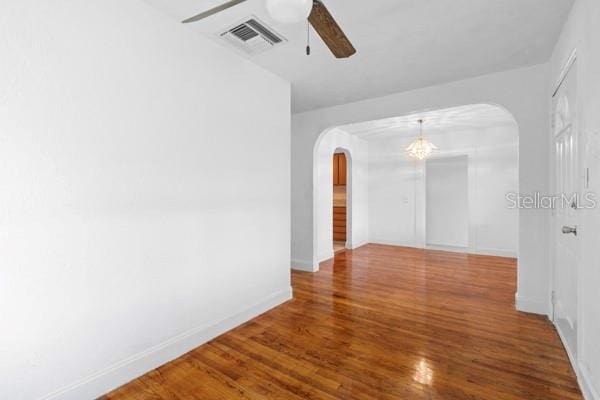 unfurnished room featuring a ceiling fan, wood finished floors, visible vents, baseboards, and arched walkways