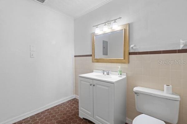 bathroom featuring toilet, crown molding, vanity, and tile walls