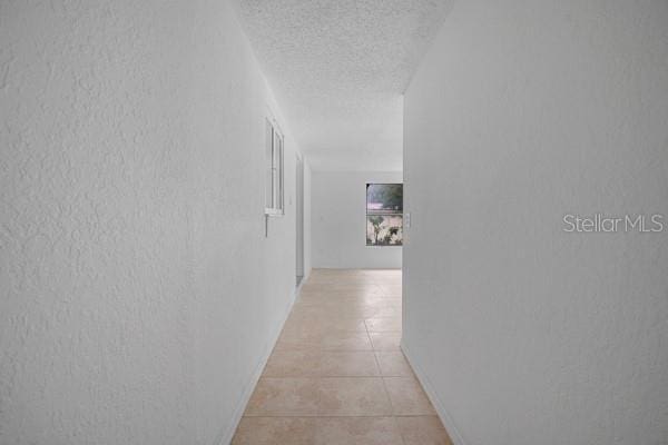 corridor with a textured ceiling, light tile patterned flooring, and a textured wall