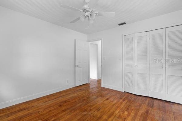 unfurnished bedroom with wood finished floors, visible vents, a closet, and baseboards