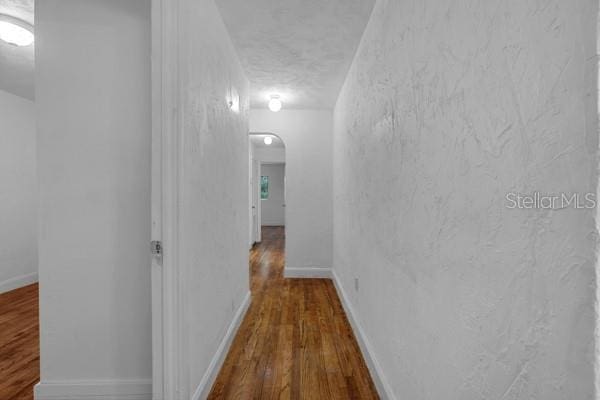 corridor with a textured ceiling, wood finished floors, baseboards, and arched walkways