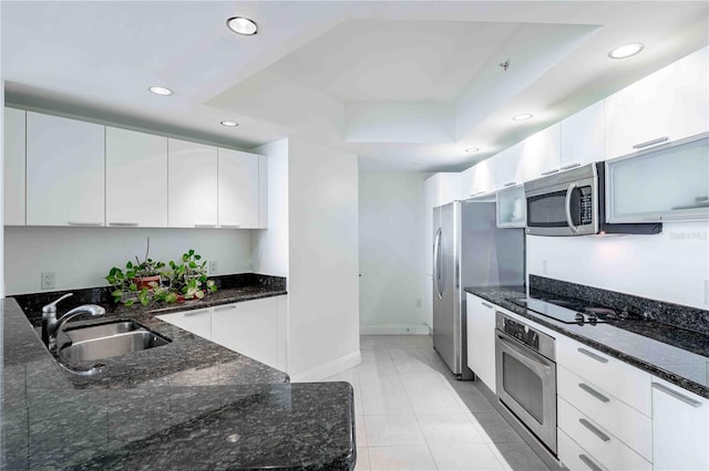 kitchen with sink, appliances with stainless steel finishes, a tray ceiling, dark stone counters, and white cabinets