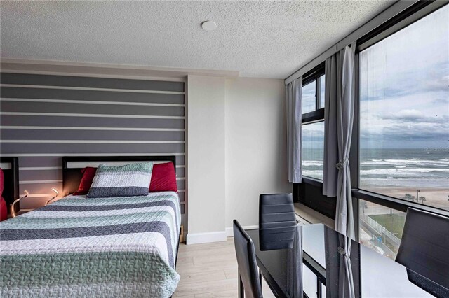 bedroom with a water view, light wood-type flooring, and a textured ceiling