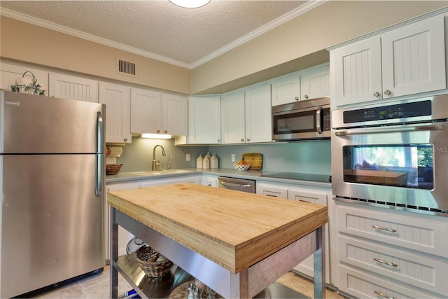 kitchen with appliances with stainless steel finishes, white cabinets, sink, light tile patterned floors, and crown molding