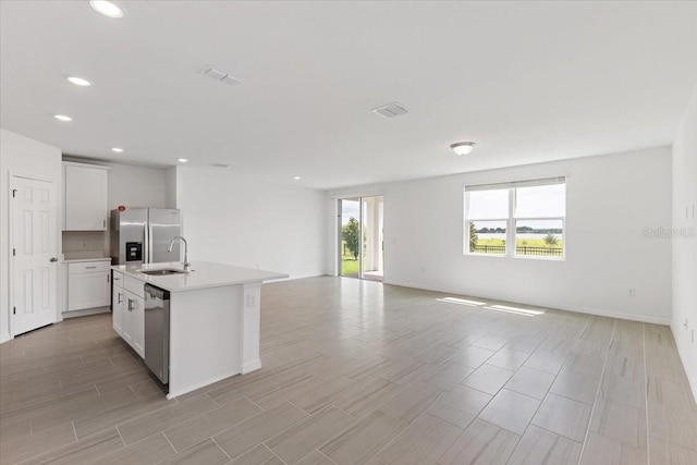 kitchen featuring white cabinetry, sink, stainless steel appliances, and an island with sink