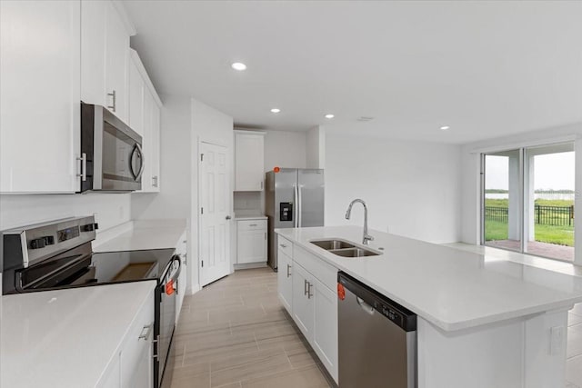 kitchen with stainless steel appliances, white cabinetry, sink, and a center island with sink