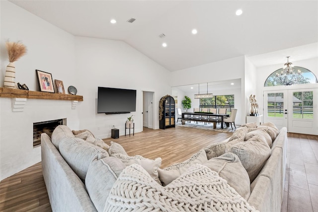 living room featuring high vaulted ceiling, light hardwood / wood-style floors, and a notable chandelier