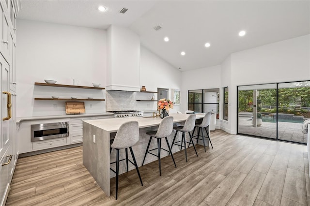 kitchen featuring light hardwood / wood-style flooring, high vaulted ceiling, a kitchen breakfast bar, an island with sink, and white cabinets