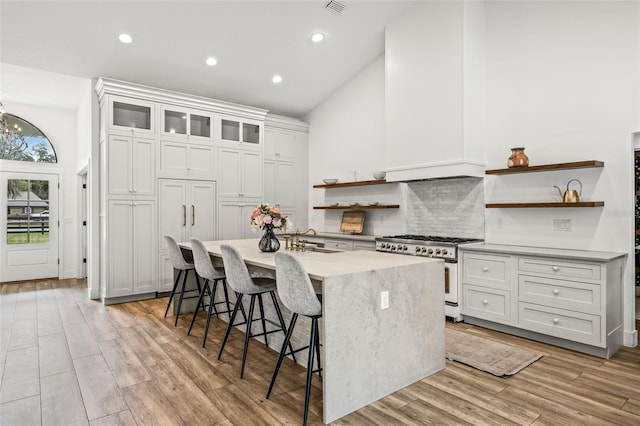 kitchen with a kitchen bar, sink, high end range, an island with sink, and white cabinets