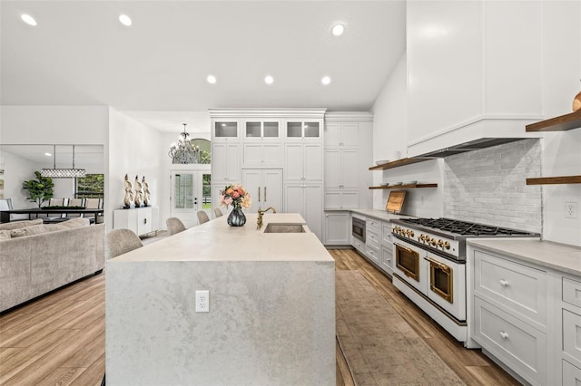 kitchen featuring sink, tasteful backsplash, an island with sink, range with two ovens, and white cabinets