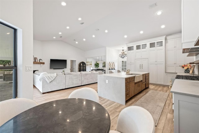 kitchen featuring lofted ceiling, sink, white cabinets, a kitchen island with sink, and light wood-type flooring