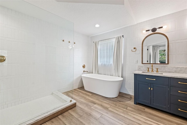 bathroom featuring a tub to relax in, wood-type flooring, tile walls, a textured ceiling, and vanity