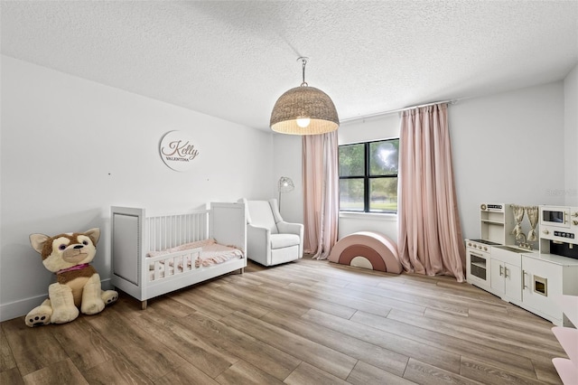 bedroom with wood-type flooring, a textured ceiling, and a crib