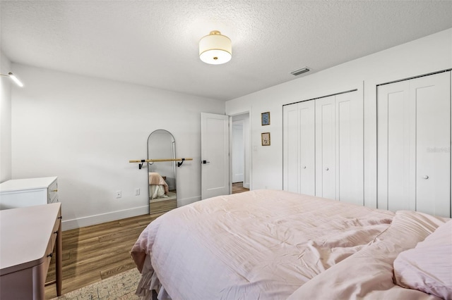 bedroom with hardwood / wood-style floors, two closets, and a textured ceiling