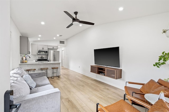 living room featuring ceiling fan, lofted ceiling, sink, and light hardwood / wood-style flooring