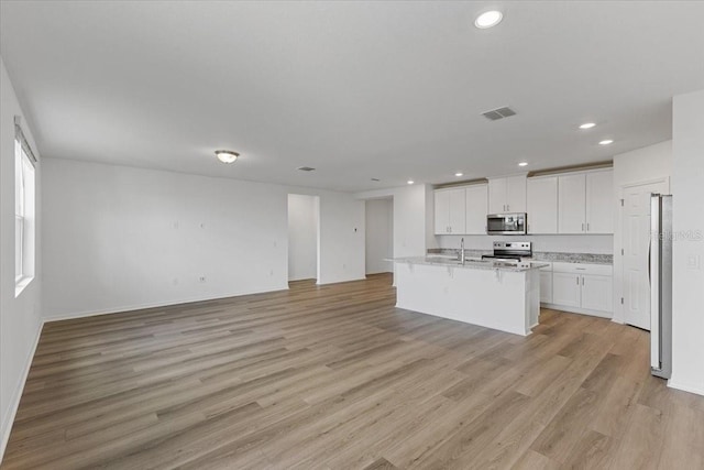 kitchen featuring white cabinetry, light stone counters, a center island with sink, light wood-type flooring, and stainless steel appliances