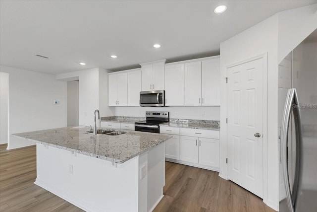 kitchen featuring sink, white cabinets, light stone counters, stainless steel appliances, and a center island with sink