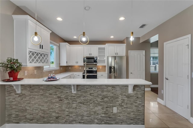 kitchen with light tile patterned floors, kitchen peninsula, stainless steel appliances, pendant lighting, and a kitchen bar