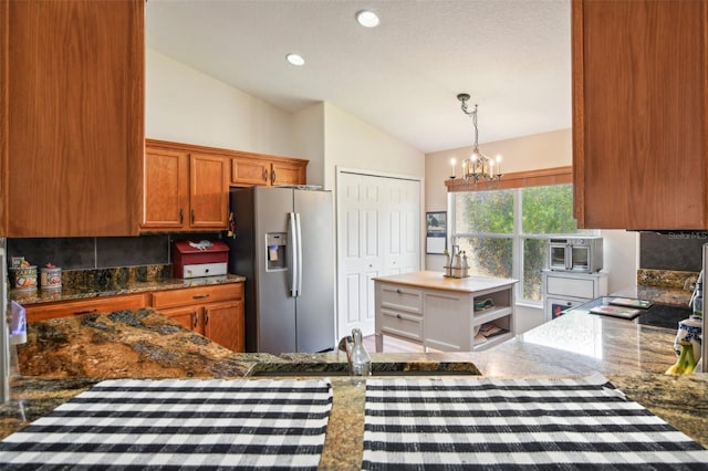 kitchen with tasteful backsplash, an inviting chandelier, vaulted ceiling, hanging light fixtures, and stainless steel fridge