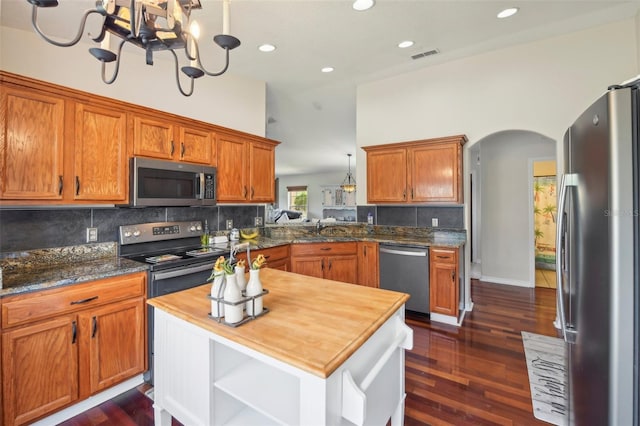 kitchen with dark hardwood / wood-style floors, decorative light fixtures, butcher block counters, kitchen peninsula, and stainless steel appliances