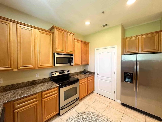 kitchen with light tile patterned floors, stainless steel appliances, and dark stone counters